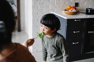 picky eater is fed vegetables by his mother